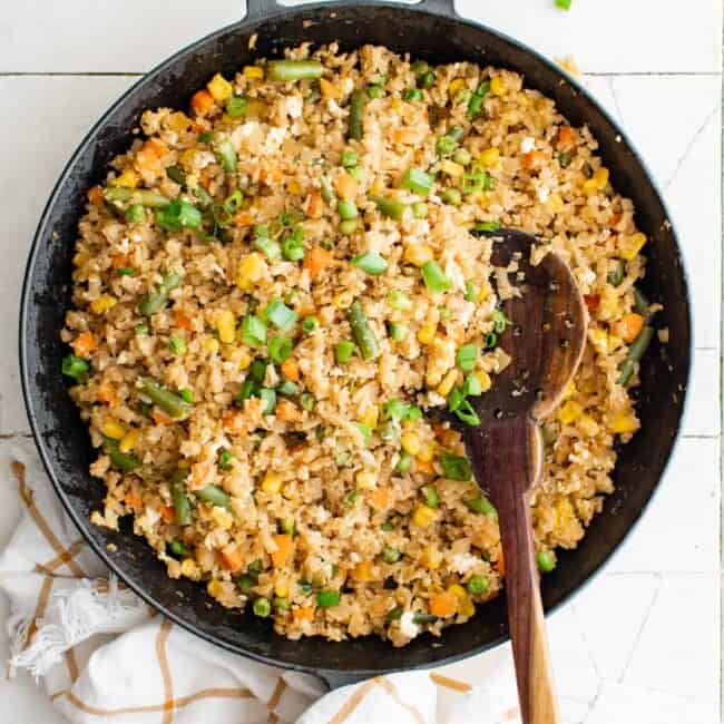 overhead view of cauliflower fried rice in a cast iron pan with a wooden spoon.