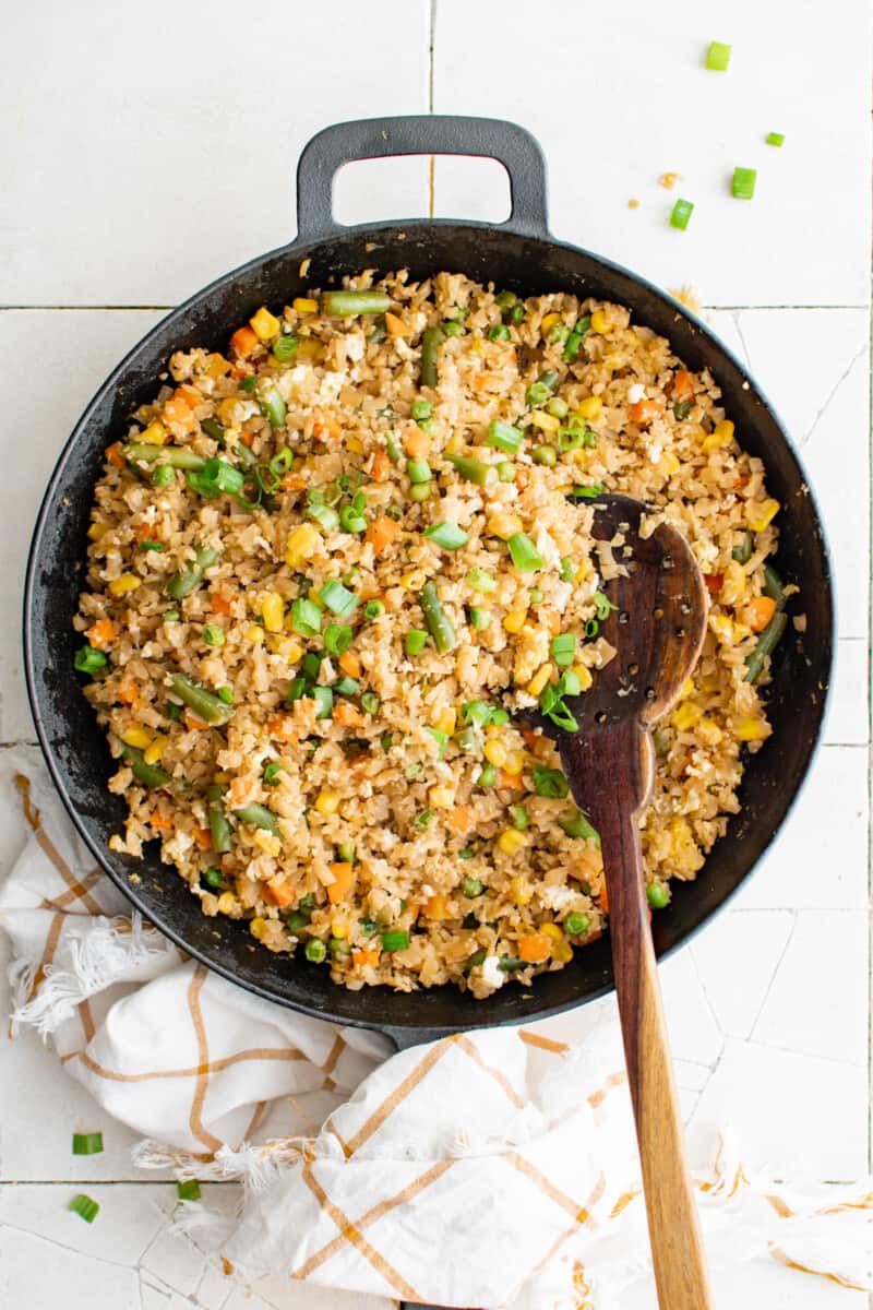 overhead view of cauliflower fried rice in a cast iron pan with a wooden spoon.
