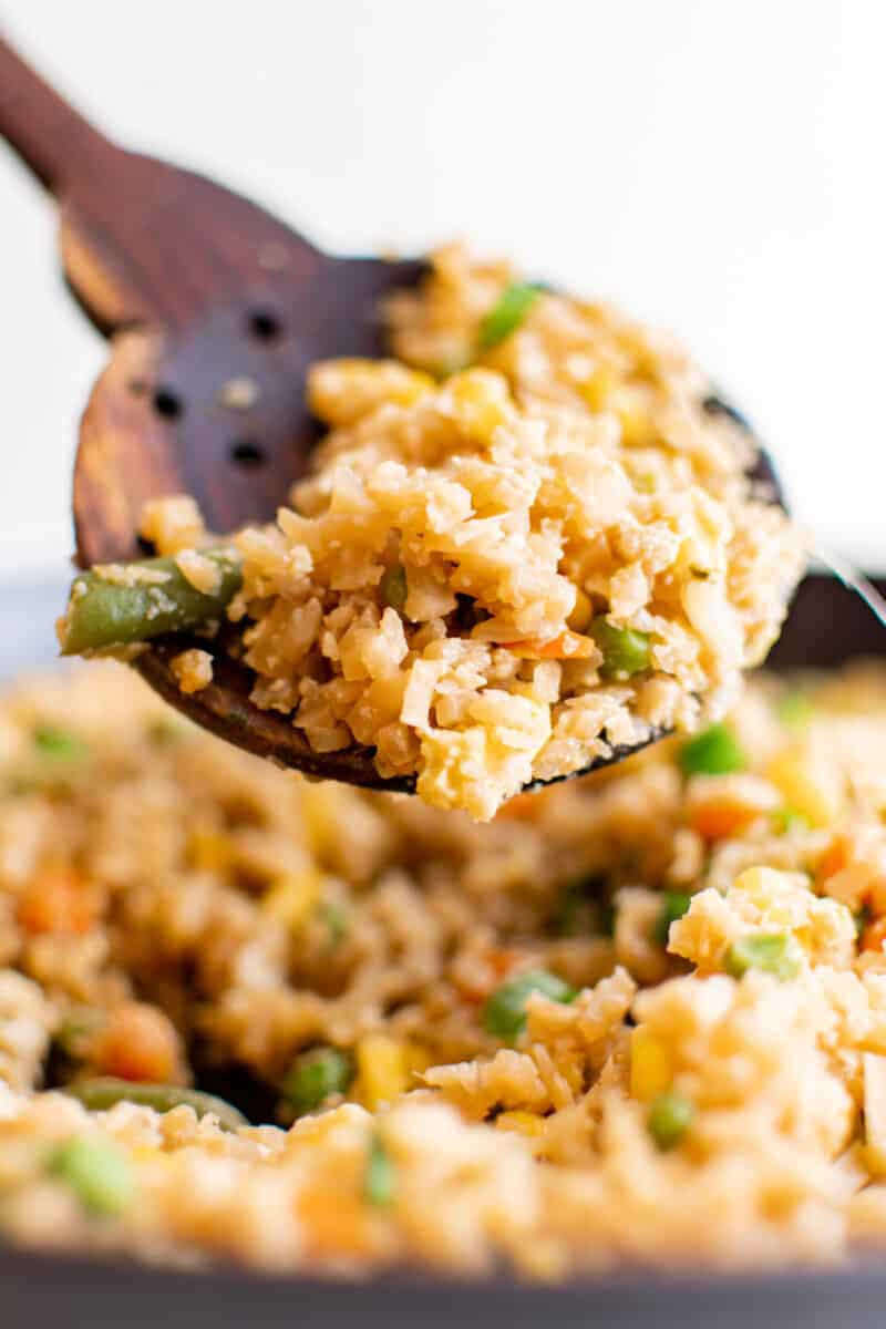 close up of cauliflower fried rice on a wooden spoon.