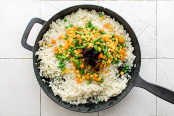 vegetables added to cauliflower rice in a cast iron pan.