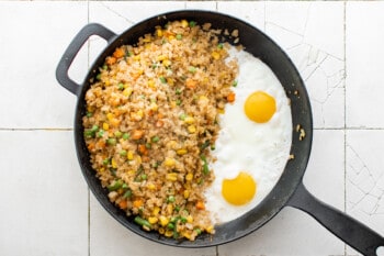 two fried eggs nestled next to cauliflower fried rice in a cast iron pan.