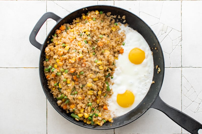 two fried eggs nestled next to cauliflower fried rice in a cast iron pan.