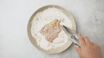 A person is kneading dough for chicken fried steak on a plate.