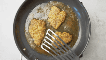 Fried chicken in a frying pan with a spatula.