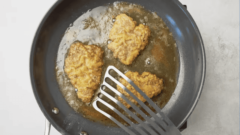Fried chicken in a frying pan with a spatula.