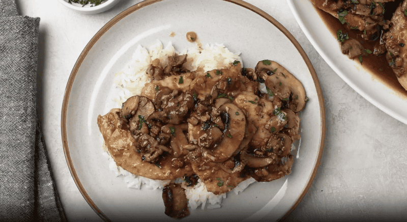 overhead view of chicken marsala over rice on a white plate.