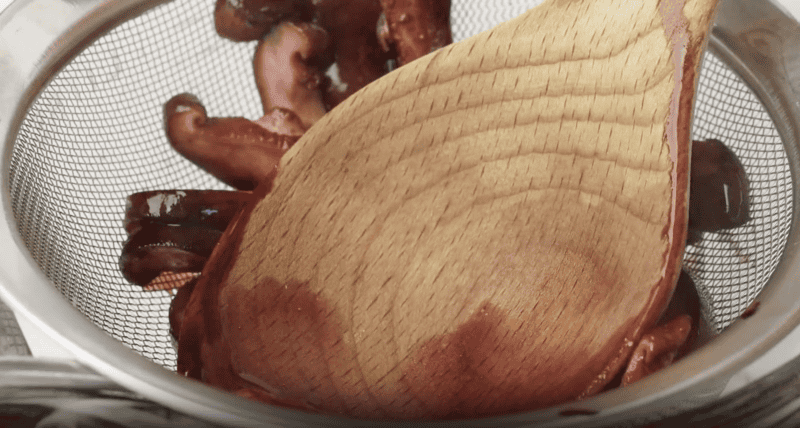 a wooden spoon pressing mushroom sauce through a mesh sieve.