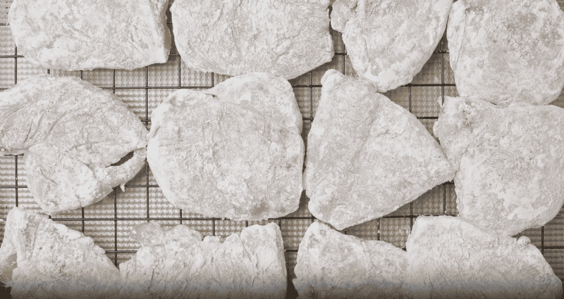 Floured chicken cutlets on a wire rack.