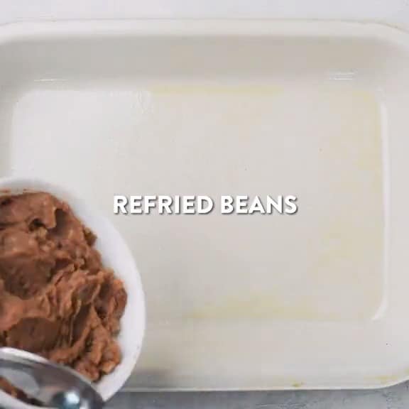 Refried beans being layered into baking pan.