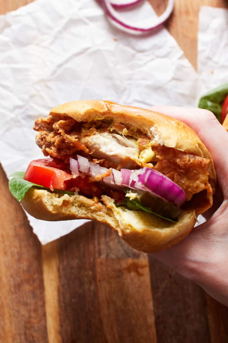 a hand holding a bitten crispy chicken sandwich upright.