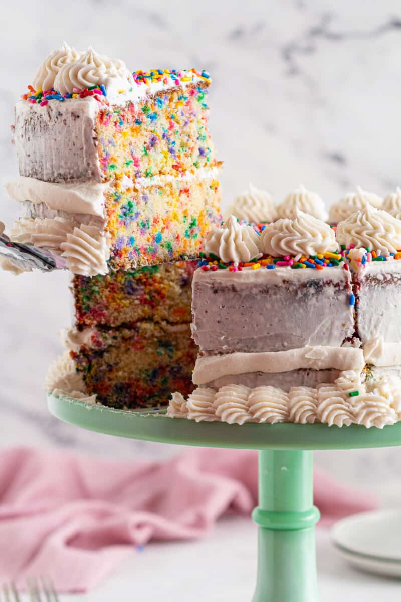 lifting slice of frosted funfetti cake on green cake stand