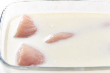 raw chicken breasts in milk in a glass baking pan.