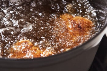 chicken breasts frying in oil in a dutch oven.