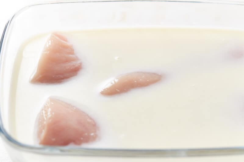 raw chicken breasts in milk in a glass baking pan.