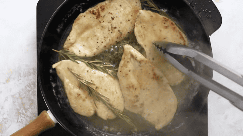 4 lemon chicken breasts in a cast iron skillet with rosemary.