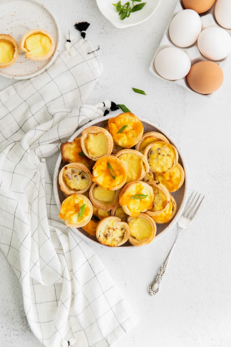 overhead view of mini quiches on a white plate with a fork and kitchen towel.