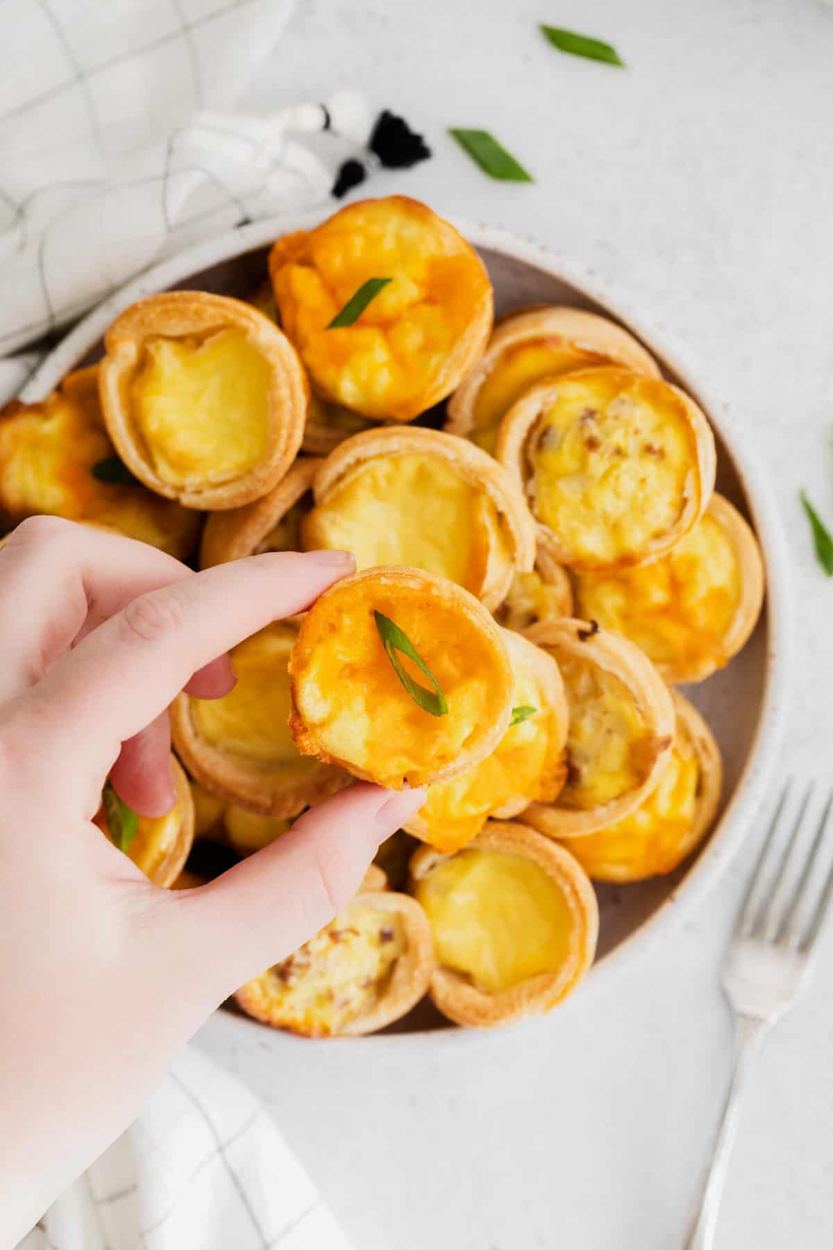 hand grabbing a mini quiche from a white plate of mini quiches.