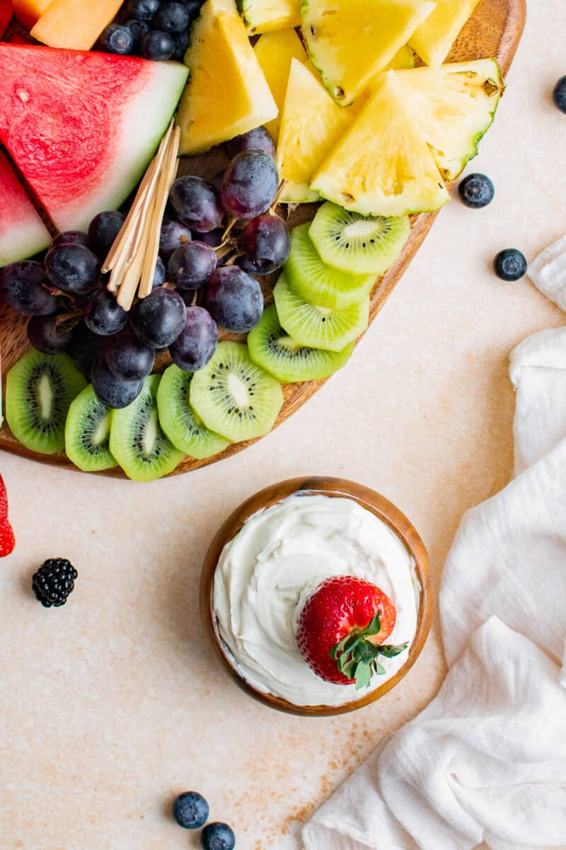 overhead strawberry dipped in cream cheese fruit dip next to fruit board