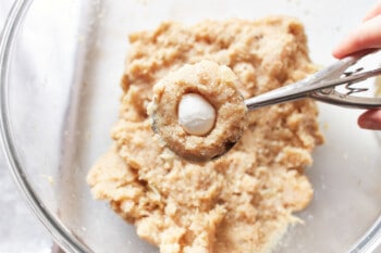 a mozzarella pearl pressed into the center of a ball of turkey meatball mixture in a cookie portion scoop.