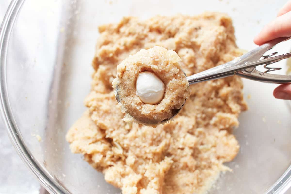 A mozzarella pearl pressed into the center of a ball of turkey meatball mixture in a cookie portion scoop.