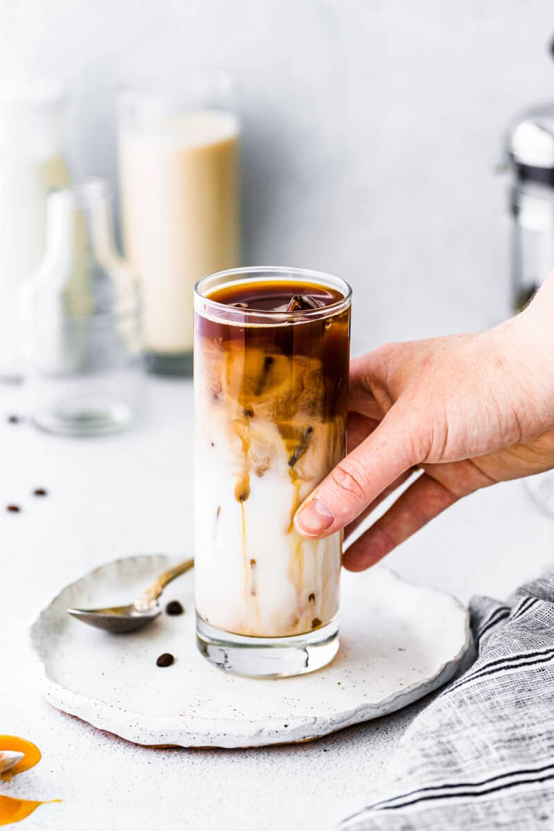 hand holding iced caramel macchiato in tall glass
