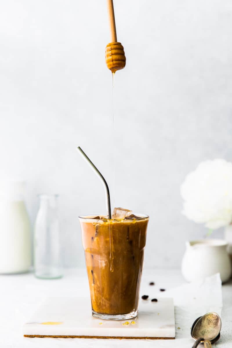 dripping honey into honey almondmilk flat white in clear glass with straw