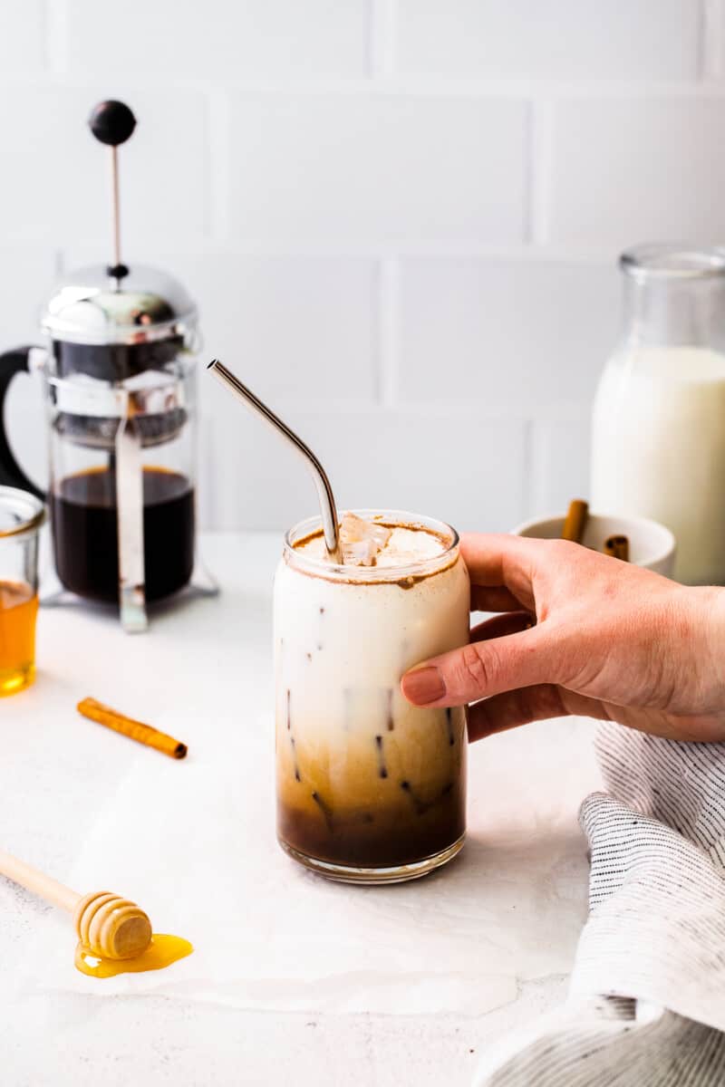 hand holding glass of iced honey cinnamon latte with metal straw