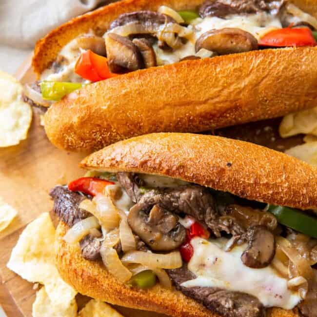 two philly cheesesteaks on cutting board