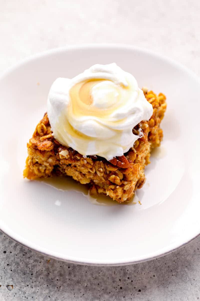 slice of pumpkin pie baked oatmeal with whipped cream and maple syrup