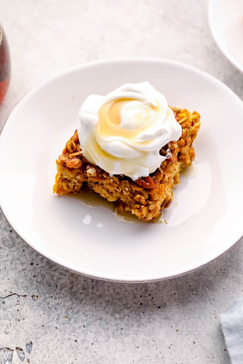slice of pumpkin pie baked oatmeal with whipped cream and maple syrup