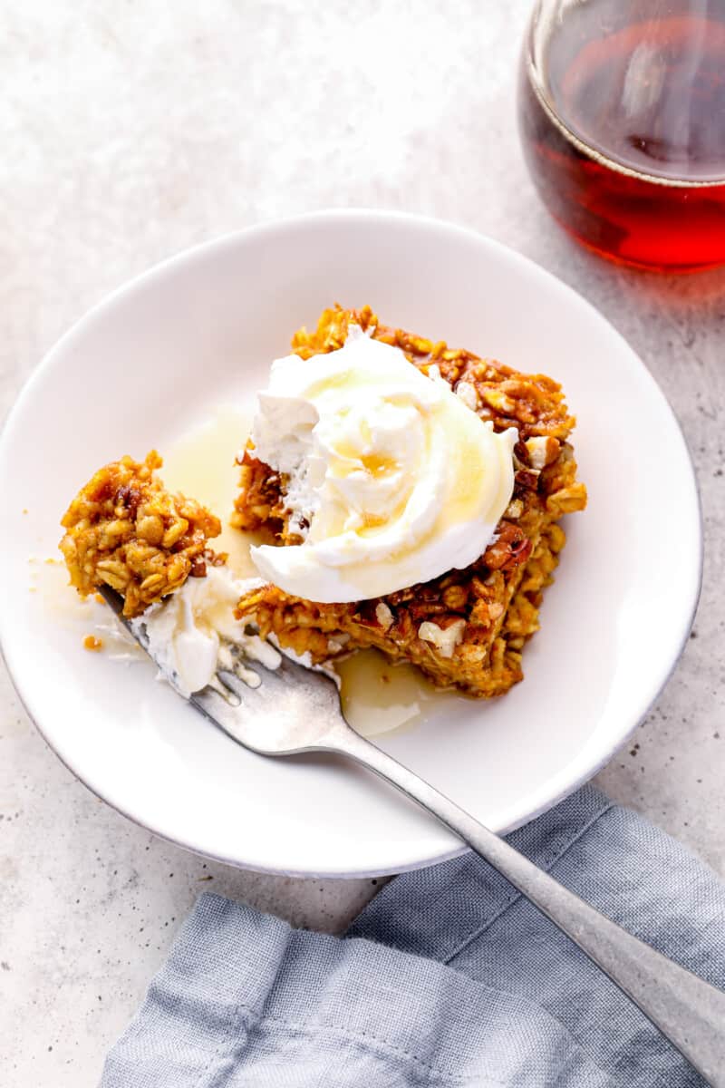 slice of pumpkin pie baked oatmeal with whipped cream and maple syrup