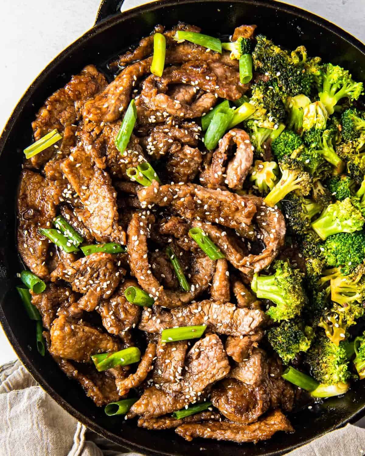 Black skillet with beef and broccoli garnished with sesame seeds. 