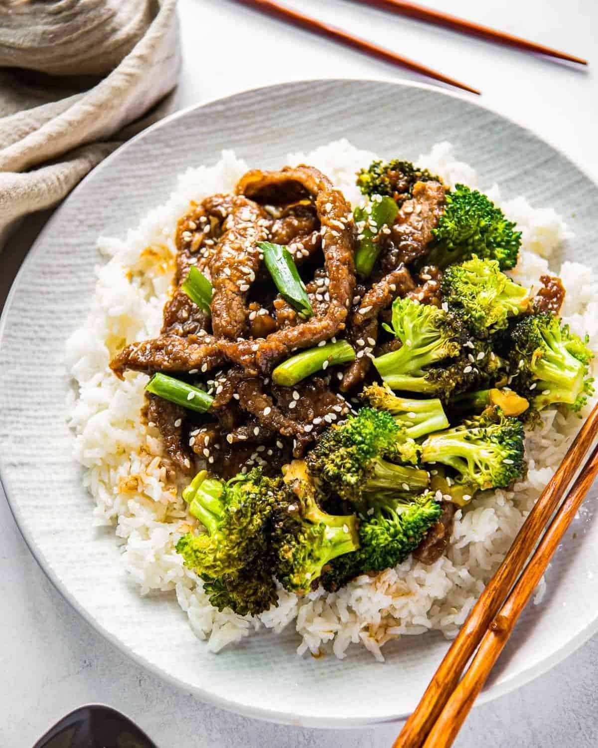 Mongolian beef and broccoli on a white plate with rice and chopsticks.