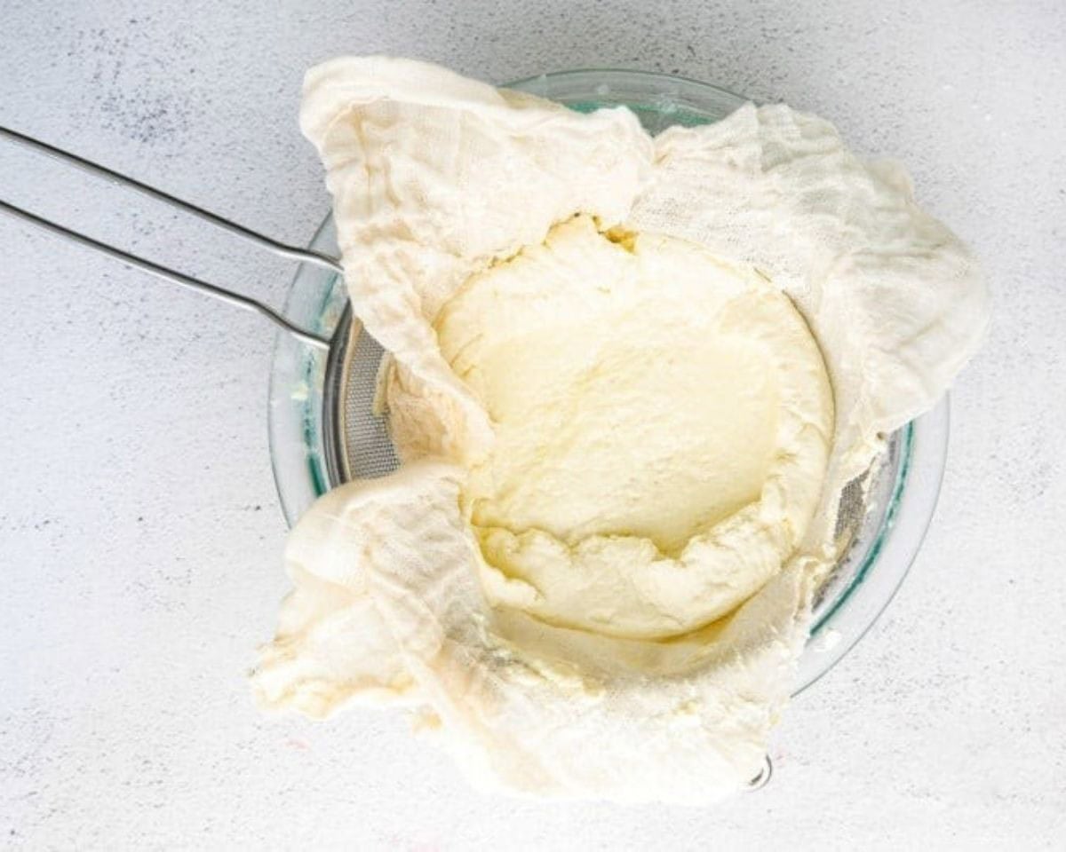 Straining the curdled milk and cream mixture through a sieve. - 8