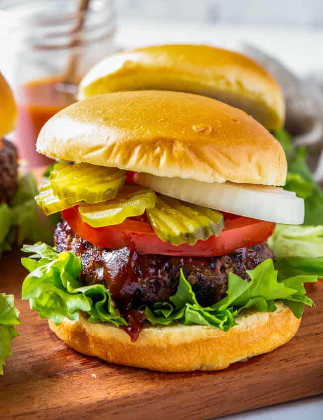 up close grilled bbq burgers with lettuce, tomato, onion, and pickles