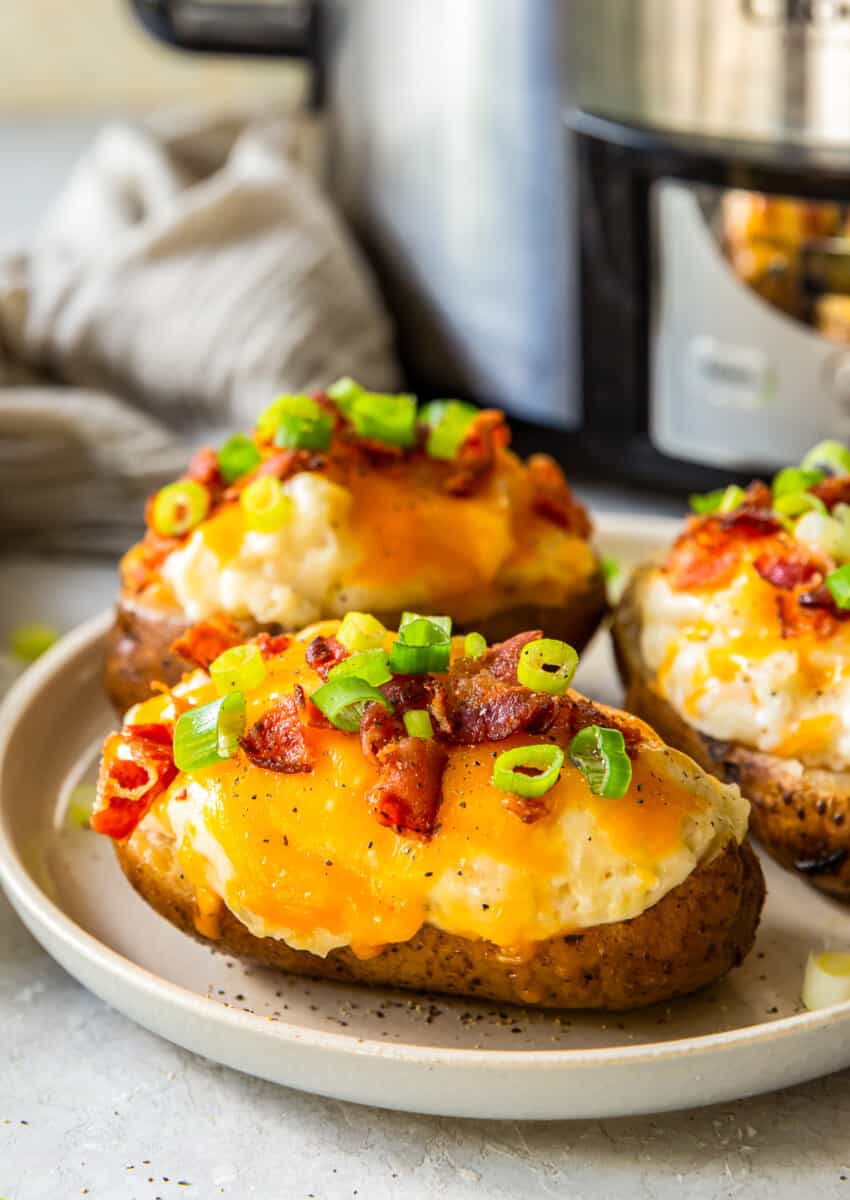 three crockpot twice baked potatoes on white plate next to slow cooker