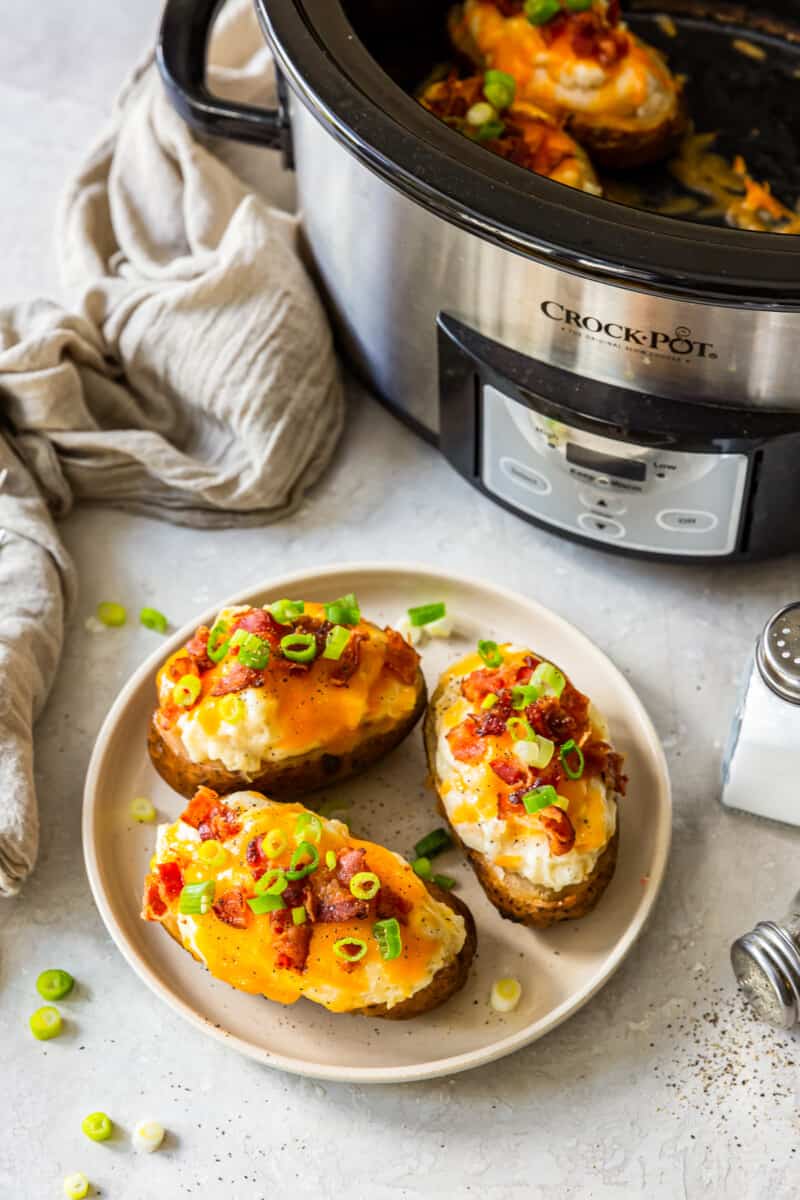 three crockpot twice baked potatoes on white plate next to slow cooker
