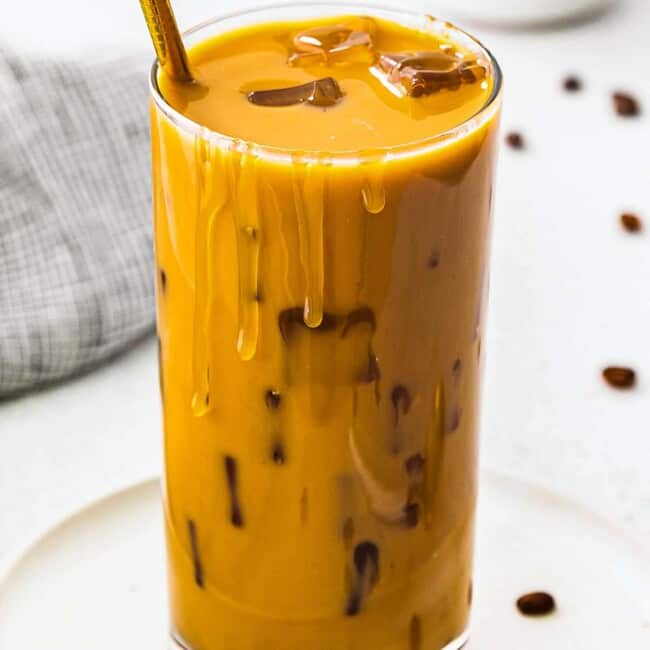 up close stirred iced caramel latte in glass with gold straw
