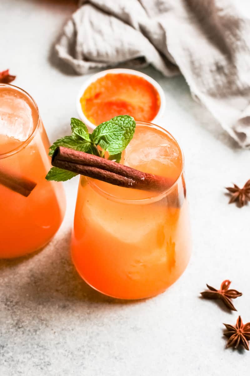 two glasses of pumpkin whiskey smash garnished with cinnamon sticks and mint