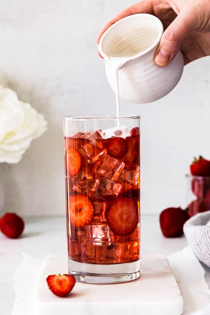 pouring cream into glass of starbucks pink drink