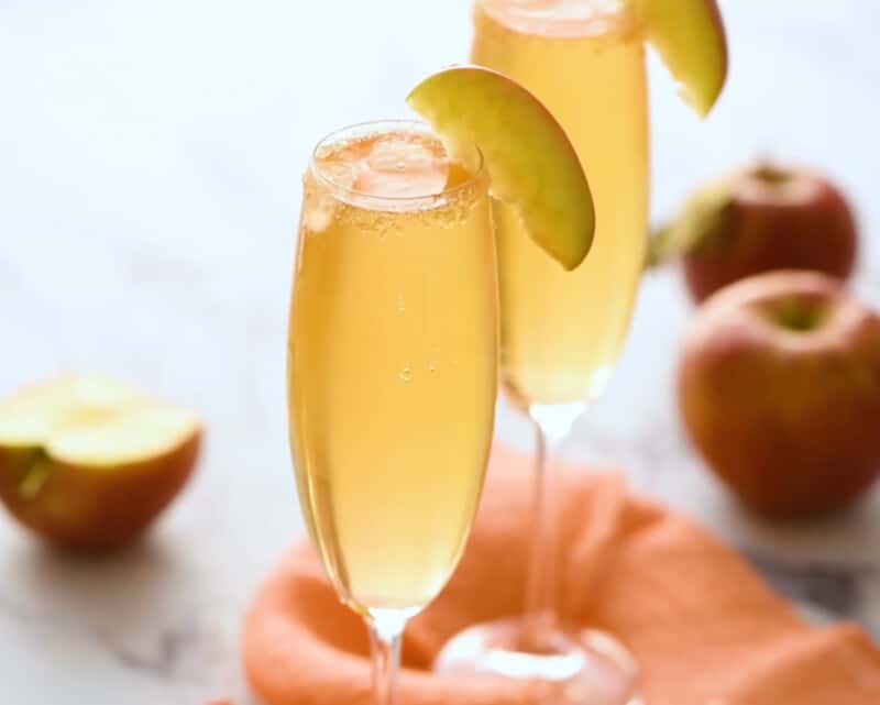 2 apple cider mimosas in glass champagne flutes garnished with apple slices