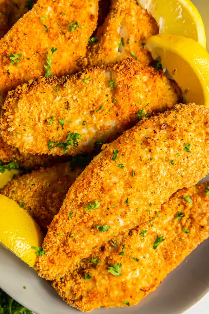 close up image of breaded tilapia filets on a platter with lemon slices