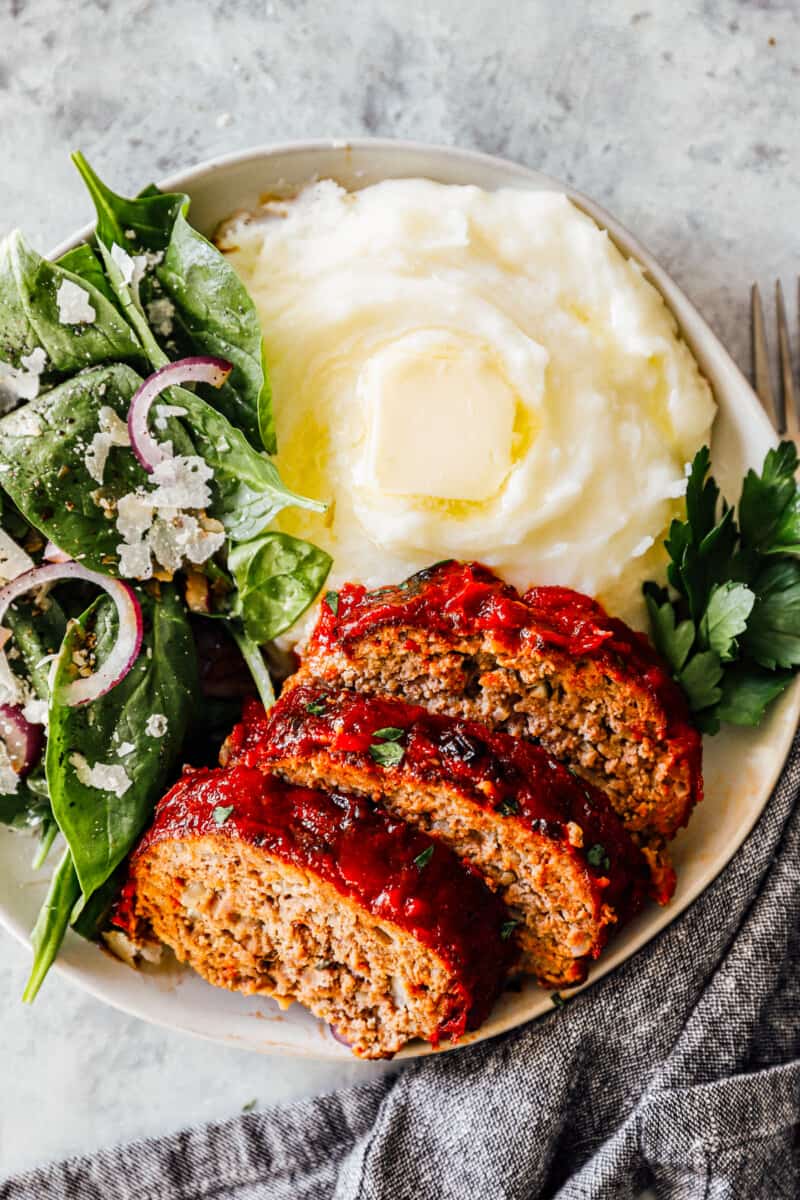 slices of air fryer meatloaf on plate with mashed potatoes and salad