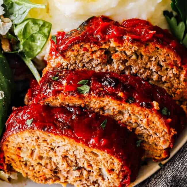 slices of air fryer meatloaf on plate with mashed potatoes and salad