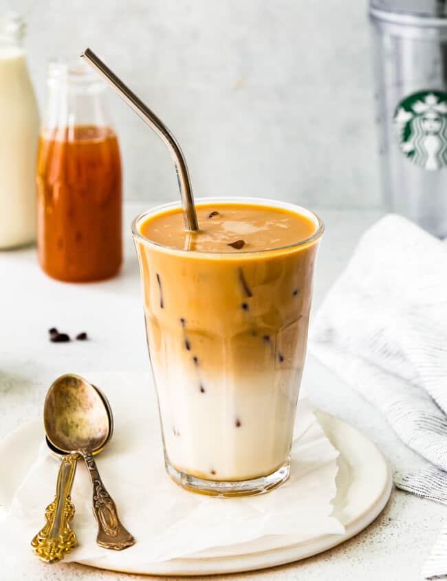 apple crisp macchiato in a clear glass on a white plate with a spoon and a straw