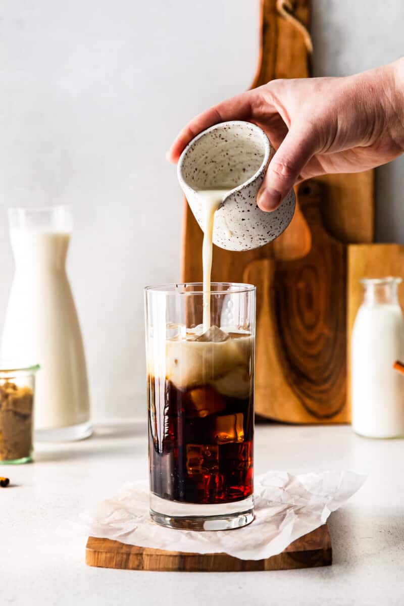 hand pouring oat milk into iced brown sugar espresso in a clear glass