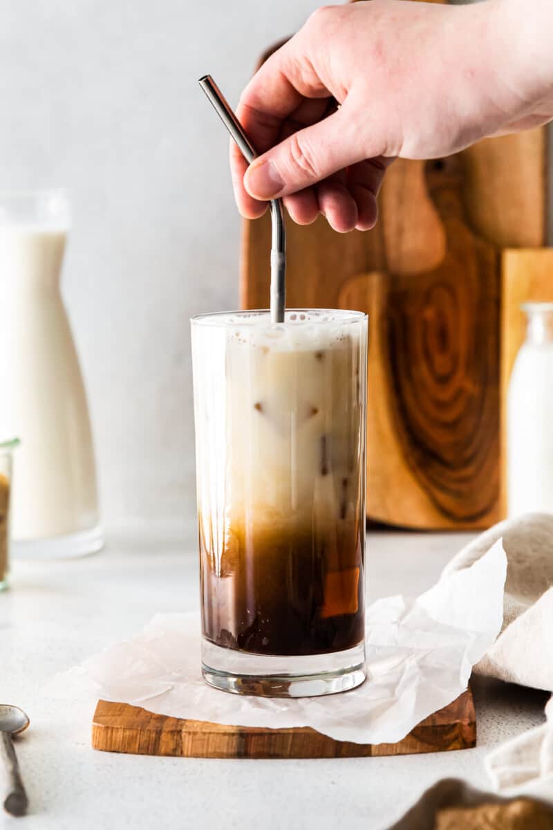hand stirring oat milk into iced brown sugar espresso in a clear glass