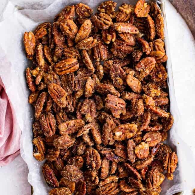 overhead image of candied pecans on a baking sheet lined with parchment paper