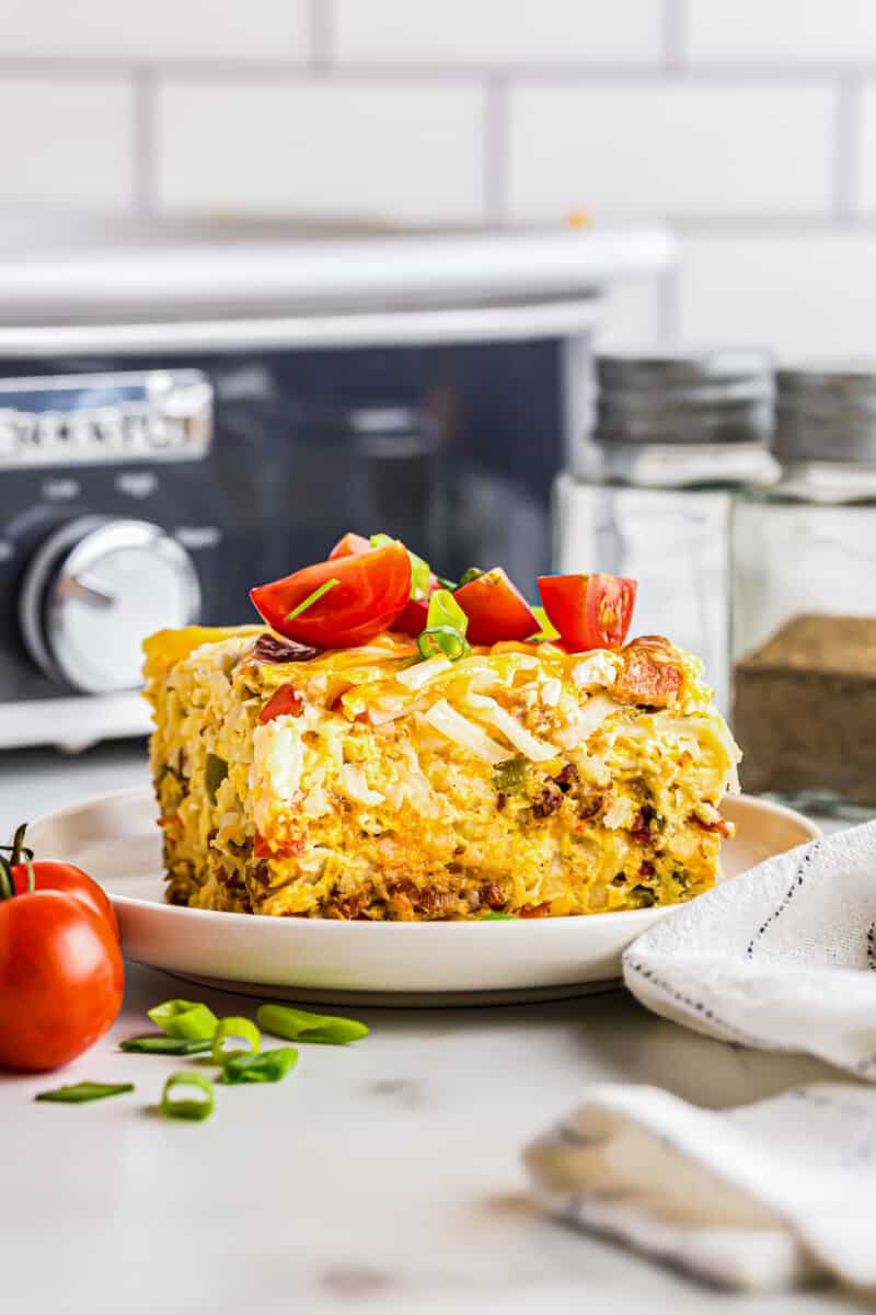 slice of breakfast casserole topped with diced tomatoes on a white plate