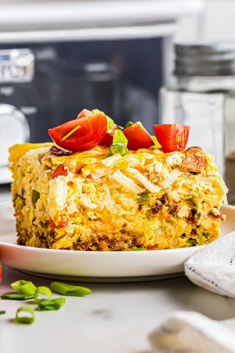 close up image of slice of breakfast casserole topped with diced tomatoes on a white plate